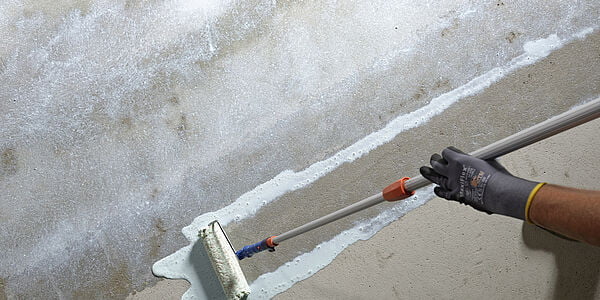 Bir kişi, beton zemine astar uygulamak için rulo kullanıyor.