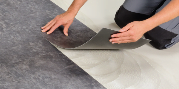 A person laying down carpet using adhesive on the floor.