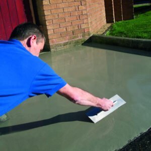 A worker applying ARDEX K 301 self-leveling screed on an outdoor surface using a trowel.