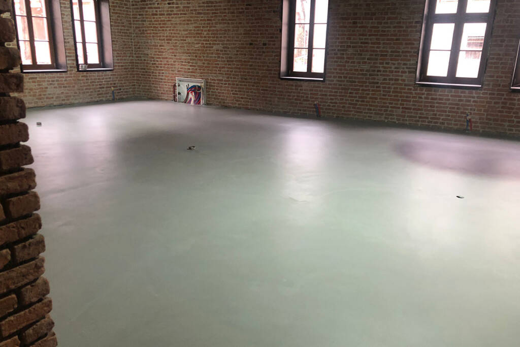Yeni döşenmiş ARDEX K511 mikrobeton zemin, tarihi tuğla duvarlı iç mekanda.