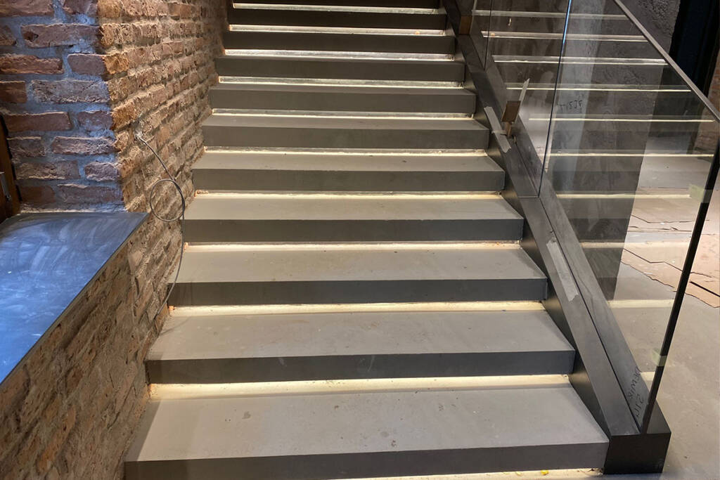 Tuğla duvarlar arasında LED aydınlatmalı modern beton merdivenler.
