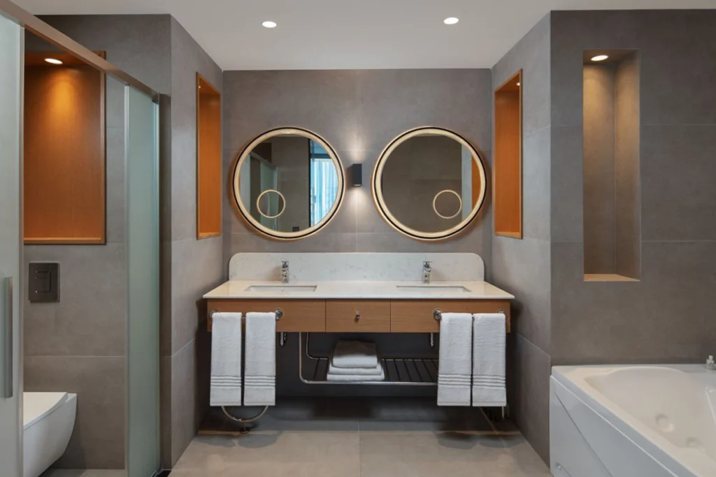 Sheraton İstanbul Esenyurt'taki lüks banyoda çift lavabo ve geniş duş alanı.